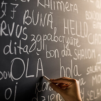 Hand schreibt mit Kreide das Wort Hallo in verschiedenen Sprachen