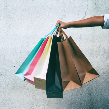 Ladies hand holds 6 shopping bags in front of concrete wall