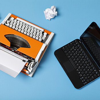 an orange typewriter with crumpled paper and a computer, photo taken from above