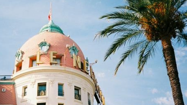 Ein Foto von einem Gebäude in Nizza und eine Palme ist zu sehen vor blauem Himmel.