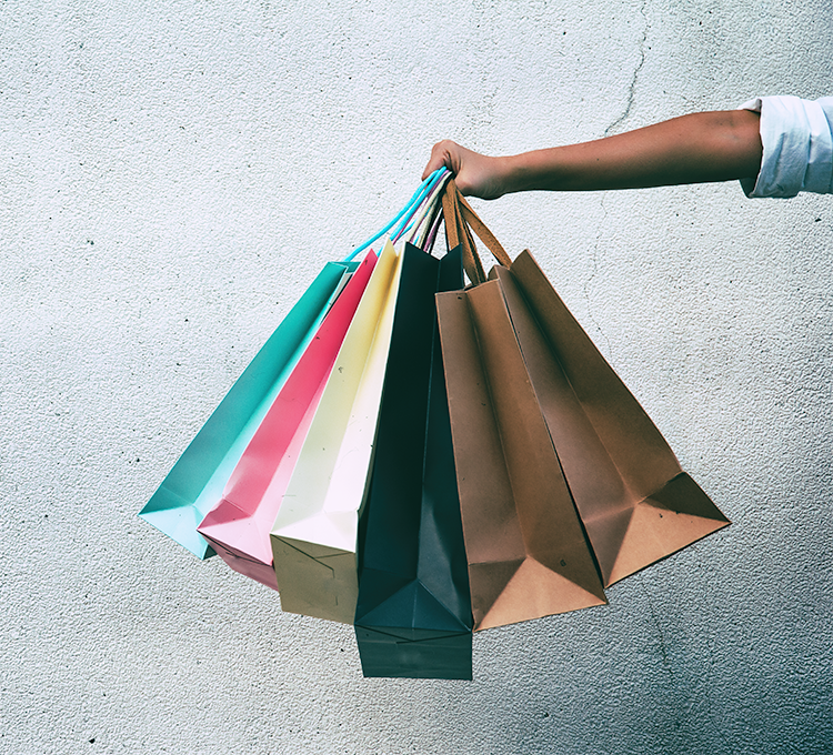 Ladies hand holds 6 shopping bags in front of concrete wall