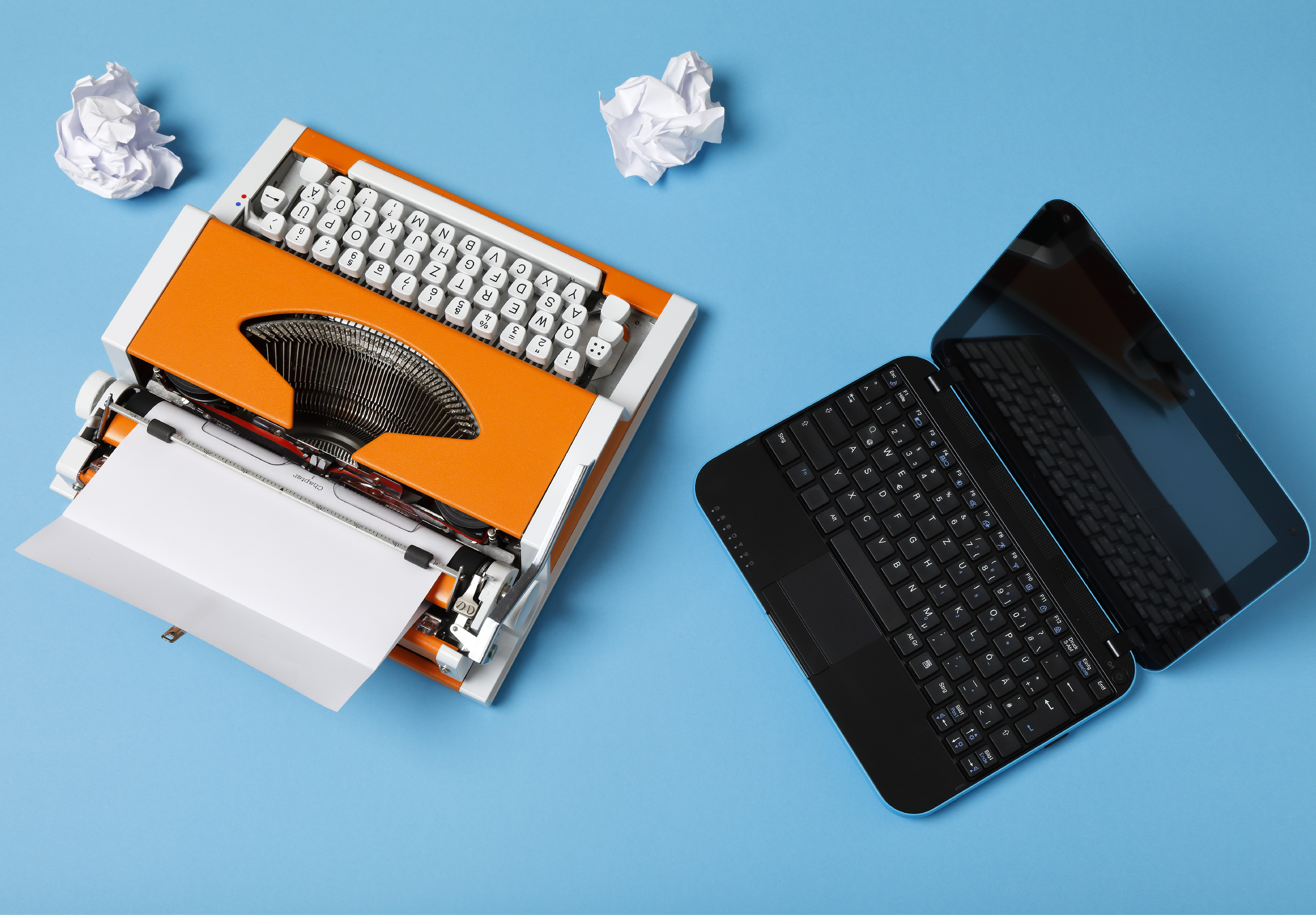 an orange typewriter with crumpled paper and a computer, photo taken from above