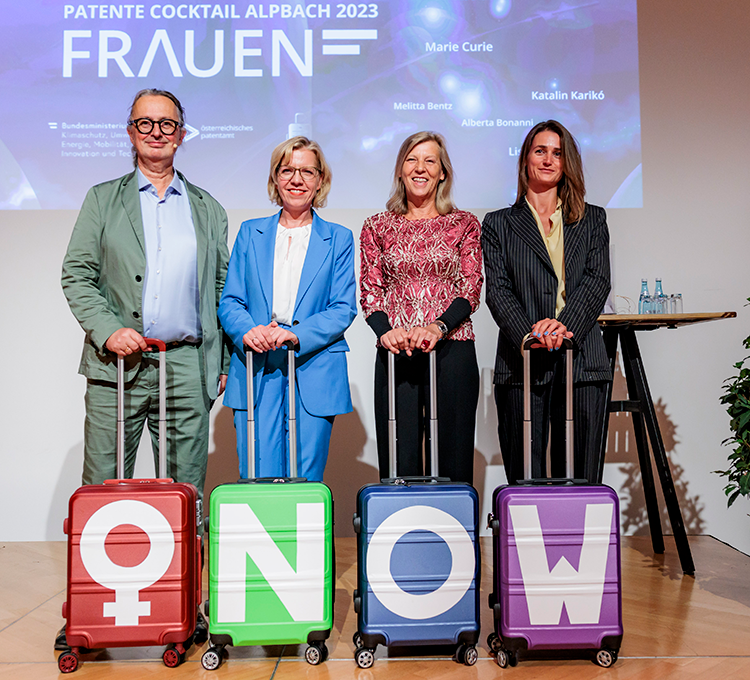 Patente Cocktail 2023 in Alpbach unter dem Motto: Patente Frauen. Auf der Bühne 1 Mann und 3 Frauen mit jeweils einem Koffer. Auf den Koffern sind Aufkleber mit dem Symbol für weibliches Geschlecht und den Buchstaben N, O und W - ergibt das wort now, englisch für jetzt. 